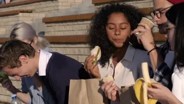 Gelukkige millennial vrienden eten sandwiches buiten. — Stockvideo