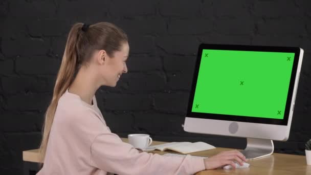 Mujer joven encantadora casual pasar tiempo en el escritorio en la oficina frente al monitor de la computadora. Pantalla verde pantalla simulada . — Vídeos de Stock
