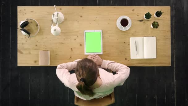 Mooi jong meisje kijken video op tablet zitten aan de balie. Groen scherm Mock-up Display. — Stockvideo