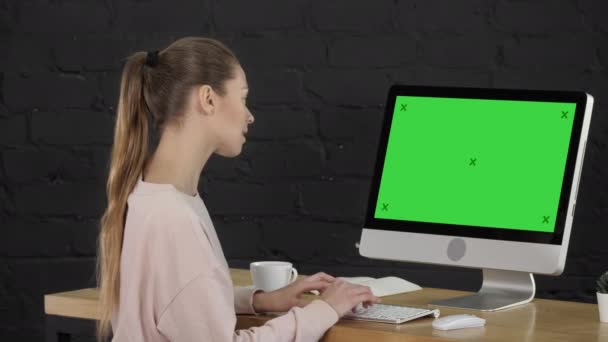 オフィスの若い女性はデスクトップコンピュータで働いています。緑の画面のモックアップ表示. — ストック動画