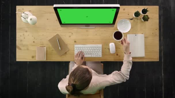 Casual businesswoman sitting on desktop with cup of coffee or tea and working on computer. Green Screen Mock-up Display. — Stock Video