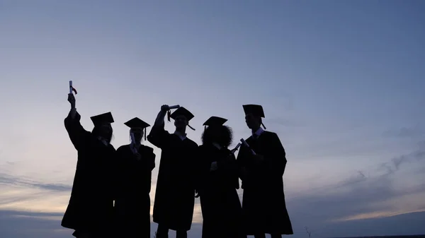Silhouette di laureati con certificati su uno sfondo di tramonto — Foto Stock