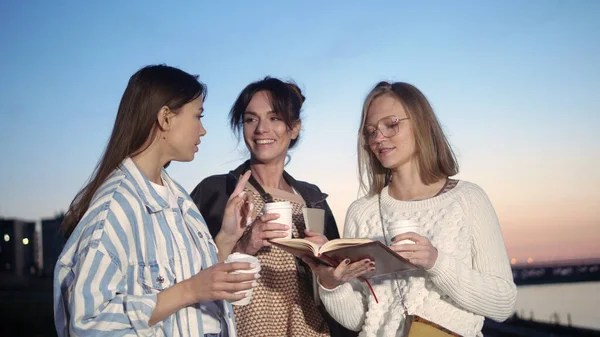 Τρεις νεαρές γυναίκες πίνουν καφέ και διαβάζουν ένα βιβλίο.. — Φωτογραφία Αρχείου