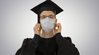 Mezuniyet cüppeli genç adam tıbbi maskeli ve değişken geçmişli..