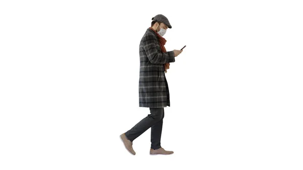 Homme en masque médical marchant et utilisant le téléphone mobile sur fond blanc . — Photo