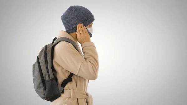 Woman wearing medical mask walking and calling someone one the phone on gradient background. — Stock Photo, Image