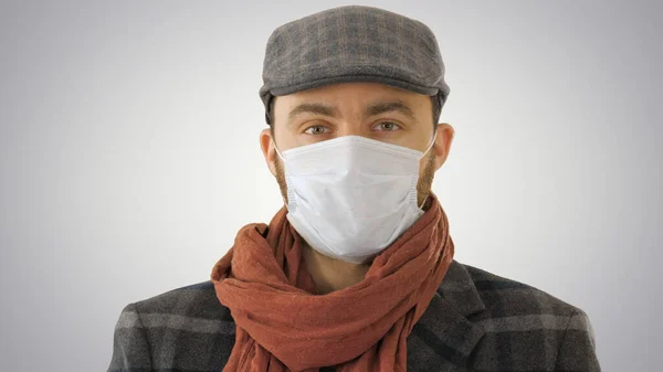 Handsome young European man in trendy coat wearing disposable protective face mask on gradient background. — Stock Photo, Image