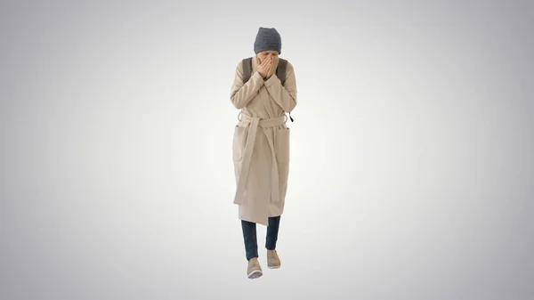 Vrouw in een jas wandelen en hoesten op gradiënt achtergrond. — Stockfoto
