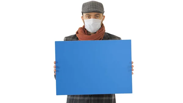 Man in een trendy outfit en medisch masker houden blanco bordje op witte achtergrond. — Stockfoto