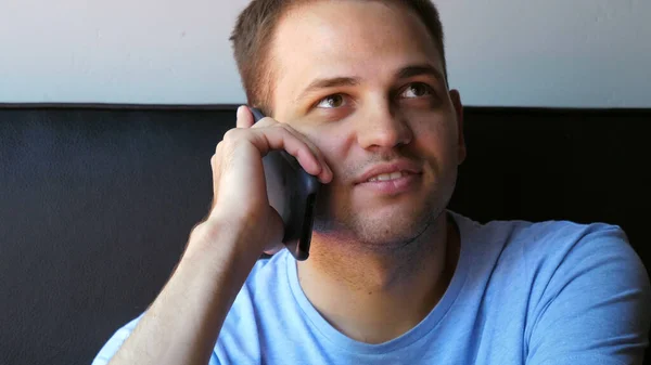 Genç ve sağlıklı bir adam evde gülümsüyor ve akıllı telefonla konuşuyor. — Stok fotoğraf