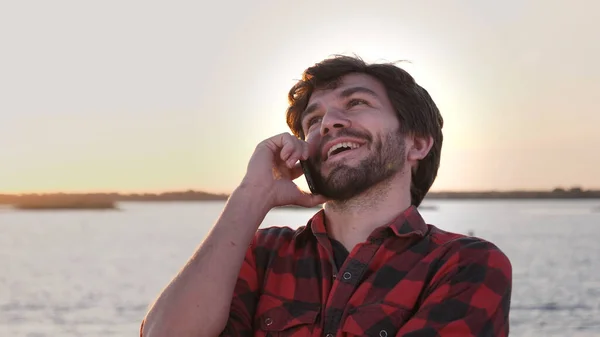 Jonge positieve vrolijke man praten door mobiele telefoon bij zonsondergang. — Stockfoto