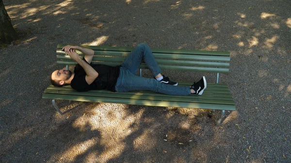 Hombre guapo acostado en el banco al aire libre y usando un teléfono inteligente. —  Fotos de Stock