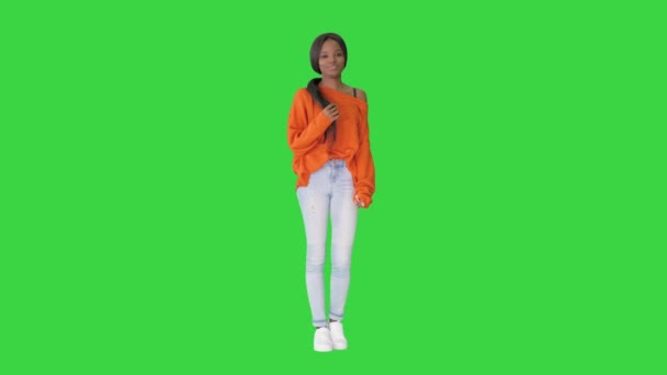 Leende afroamerikansk kvinna klädd i ljus tröja och jeans poserar med händerna i fickor på en grön skärm, Chroma Key. — Stockvideo