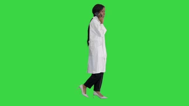 緑の画面、クロマキーを歩いている間に電話で話すアフリカ系アメリカ人女性医師. — ストック動画
