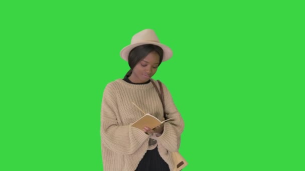 Mujer afroamericana bonita en suéter de punto y sombrero escribiendo en su bloc de notas en una pantalla verde, Chroma Key . — Vídeos de Stock