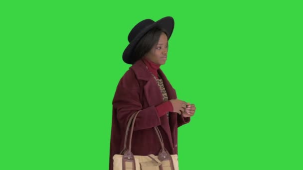 Menina da moda afro-americana em casaco e chapéu preto posando com uma bolsa em uma tela verde, Chroma Key . — Vídeo de Stock