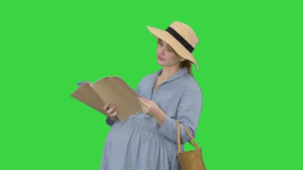 Schwangere Frau mit Sommerhut liest Magazin auf einem Green Screen, Chroma Key. — Stockvideo