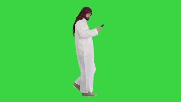 Arabischer Mann, der mit seinem Smartphone im Internet surft oder Nachrichten verschickt, während er auf einem Green Screen läuft, Chroma Key. — Stockvideo