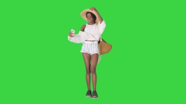 Saman şapkalı gülümseyen Afrikalı Amerikalı kadın yeşil ekranda yürürken selfie çekiyor, Chroma Key.
