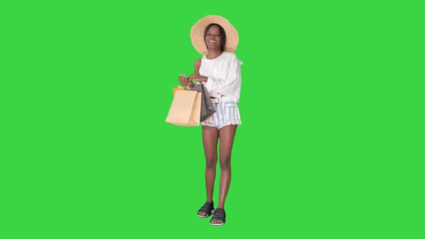Glimlachende Afro-Amerikaanse vrouw met strohoed poseren met boodschappentassen op een groen scherm, Chroma Key. — Stockvideo