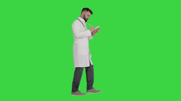 Γιατρός ή τραυματιοφορέας κρατώντας στυλό και σημειωματάριο ψάχνει για ιδέα, ενώ το περπάτημα σε μια πράσινη οθόνη, Chroma Key. — Αρχείο Βίντεο