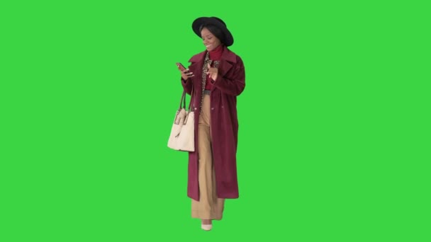 Aantrekkelijke vrouw modieuze winter outfit sms-bericht met haar telefoon als ze loopt op een groen scherm, Chroma Key. — Stockvideo