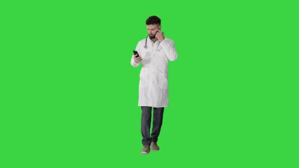Muž lékař v bílé lékařské uniformě chůze a pomocí smartphone na zelené obrazovce, Chroma Key. — Stock video