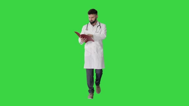 Doctor reading a book or a journal while walking on a Green Screen, Chroma Key. — Stock Video