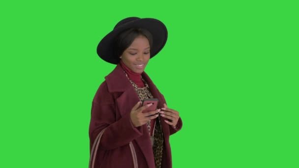 Menina de moda afro-americana bonita em casaco e chapéu preto mensagens de texto em seu telefone enquanto caminhava em uma tela verde, Chroma Key . — Vídeo de Stock