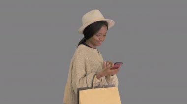 Büyük beden kazaklı ve şapkalı mutlu Afrikalı Amerikalı moda kızı yürürken telefonuna mesaj atıyor, Alpha Channel.