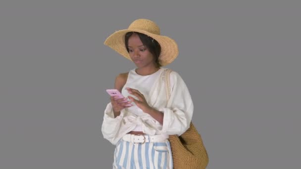 Sonriendo joven afroamericana mujer en un sombrero de paja mensajes de texto en su teléfono, Alpha Channel — Vídeo de stock