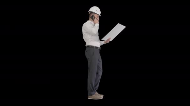 Инженер в формальной одежде и каскаде разговаривает с клиентом или подрядчиком на мобильном телефоне и смотрит на чертеж, Альфа-канал — стоковое видео