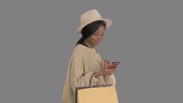 Happy African American Fashion Girl w dzianiny przerośnięty sweter i kapelusz smsowanie na jej telefon podczas spaceru, Alpha Channel — Wideo stockowe