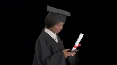 Gülümseyen Afro-Amerikan kadın mezun yürürken telefonunda diplomasıyla mesajlaşıyor, Alpha Channel.