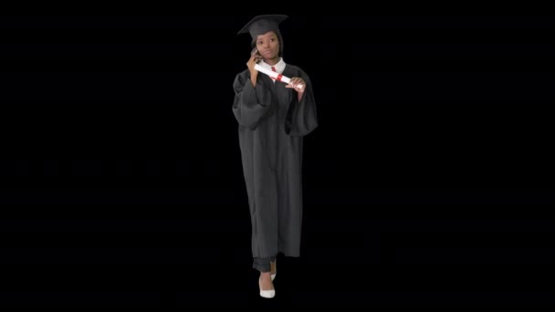 Afro-americana estudiante en bata de graduación hablando por teléfono mientras camina, Alpha Channel — Vídeos de Stock