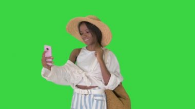 Gülümseyen Afrikalı Amerikalı kadın hasır şapka takıyor ve yeşil ekranda akıllı telefondan selfie çekiyor, Chroma Key..