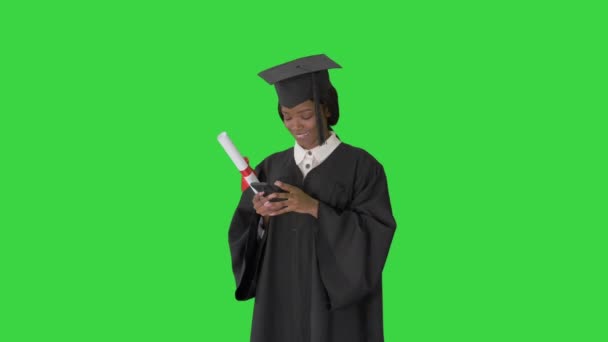 Boldog afro-amerikai női diplomás kezében diploma és SMS-t a telefonján egy zöld képernyőn, Chroma Key. — Stock videók