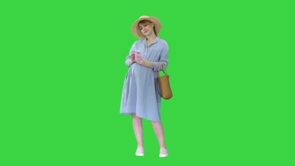 Mujer embarazada feliz en vestido azul y sombrero usando su teléfono inteligente en una pantalla verde, Chroma Key . — Vídeos de Stock