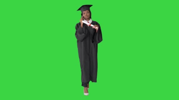Afrikai amerikai diáklány ballagási köntösben beszél telefonon, miközben sétál a zöld képernyőn, Chroma Key. — Stock videók