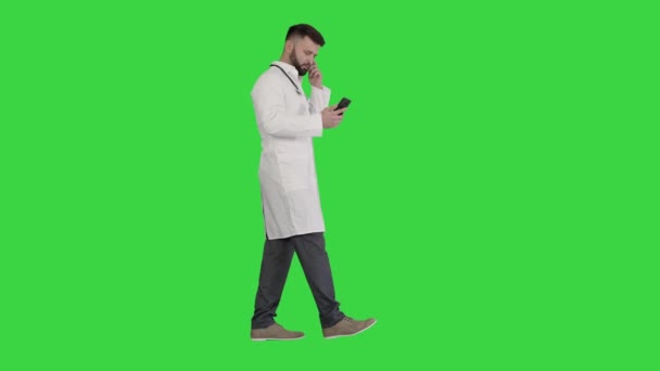 Médico masculino en uniforme médico blanco caminando y usando teléfono inteligente en una pantalla verde, Chroma Key . — Vídeos de Stock