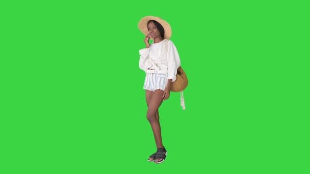 Uma jovem afro-americana bonita com um chapéu de palha a falar no telemóvel numa tela verde, Chroma Key. — Vídeo de Stock