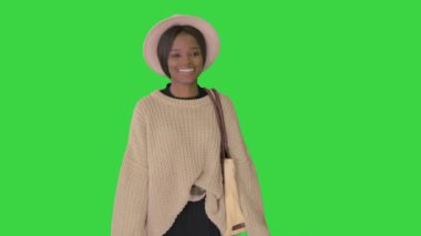 Örgü ve beyaz şapkalı gülümseyen Afrikalı Amerikalı kadın yeşil ekranda yürürken poz veriyor, Chroma Key.