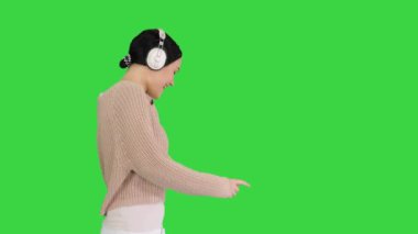 Gülümseyen kadın kulaklıklarla yürüyor ve yeşil ekrandaki müziğin tadını çıkarıyor, Chroma Key.