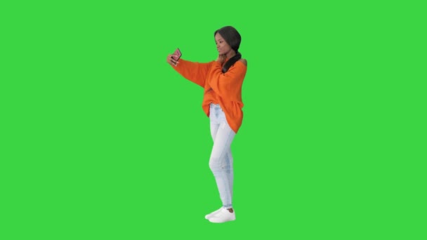 Усміхнена афро-американська жінка в яскравому джемпер робить сельфі і перевіряє свій телефон на зеленому екрані, Chroma Key. — стокове відео