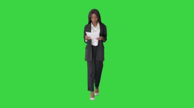 Ciddi bir Afrikalı Amerikalı kadın yeşil ekranda yürürken belge okuyor, Chroma Key.