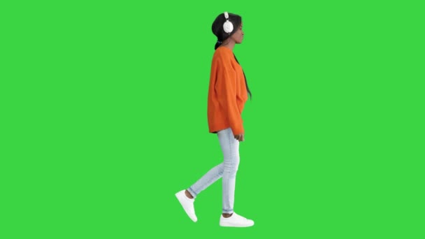 ヘッドフォンでアフリカ系アメリカ人女性の笑顔緑の画面上の音楽を聞いて歩く,クロマキー. — ストック動画