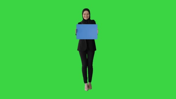 빈 파란색 포스터를 들고 녹색 화면, 크로마 키 (Chroma Key) 에서 카메라를 보고 히잡을 입은 아랍 여성. — 비디오