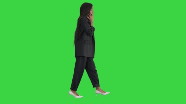 緑の画面、クロマキーを歩いている間に電話で話すカジュアルなアフリカ系アメリカ人のビジネスマンの女性. — ストック動画