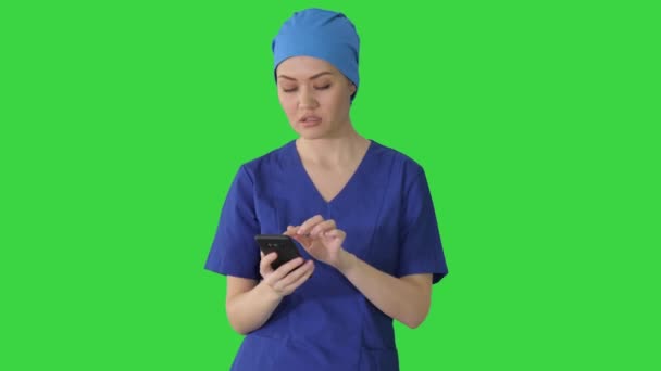 Ärztin oder Krankenschwester in blauer Uniform mit ihrem Handy, während sie auf einem grünen Bildschirm läuft, Chroma Key. — Stockvideo