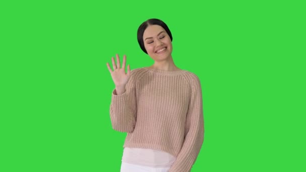 笑顔の若い女性がグリーンスクリーン、クロマキーのカメラを見て挨拶として彼女の手を振って. — ストック動画